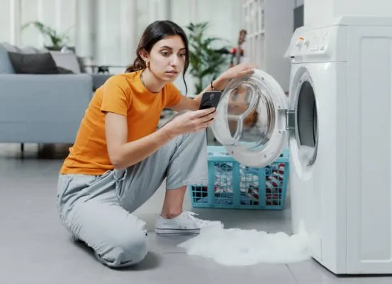 Imagen que muestra a una mujer con playera naranja solicitando por medio de su celular la ayuda de un servicio de reparación de lavadora Samsung