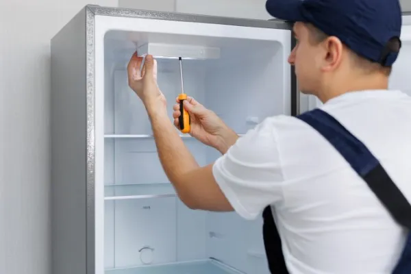 Un hombre de uniforme repara la luz del refrigerador marca Samsung con un destornillador, está sustituyendo la bombilla