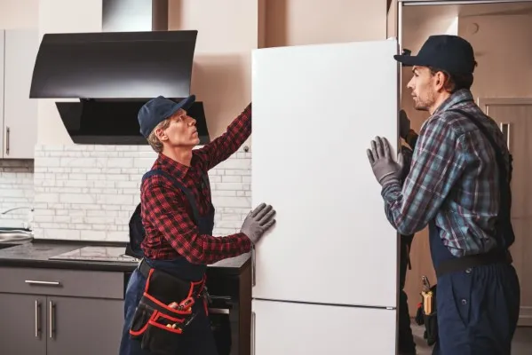 Dos trabajadores del equipo de reparación de refrigeradores marca Samsung están realizando un servicio y tienen que mover el refrigerador.