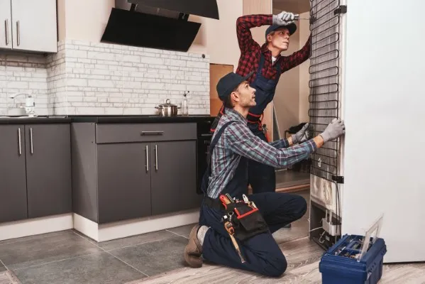 Dos trabajadores jóvenes revisando el refrigerador Samsung del que recibieron una solicitud de servicio de reparación de refrigeradores