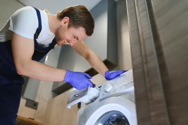 Las manos de un hombre que acaba de abrir una lavadora para revidarla y realizarle un servicio de reparación de lavadoras marca Mabe