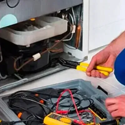 Técnico reparando el motor de un refrigerador con herramientas profesionales, servicio especializado en reparación de línea blanca como refrigeradores de diferentes marcas.