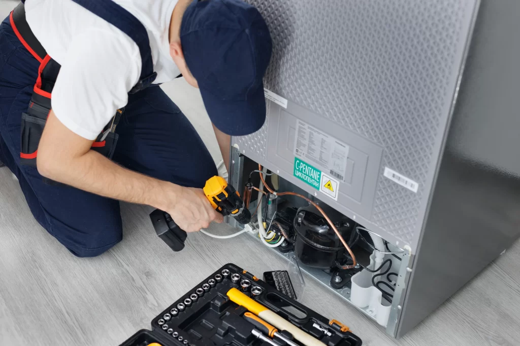 Hombre revisa motor de refrigerador para resolver ¿Por qué mi refrigerador LG no enfría pero sí prende? Causas y soluciones