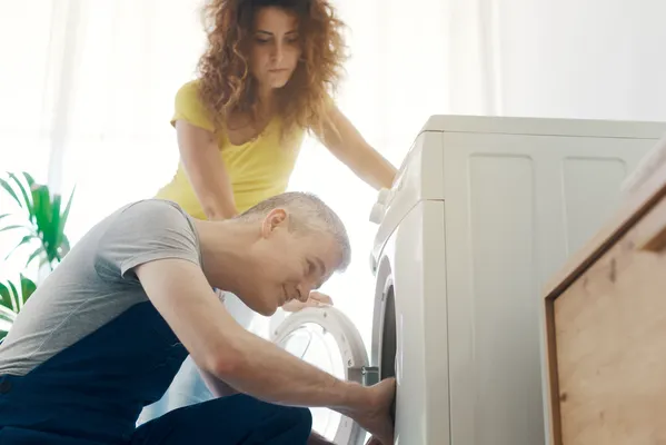 Hombre revisa el interior de una lavadora LG hace ruido fuerte, mientras una mujer observa.