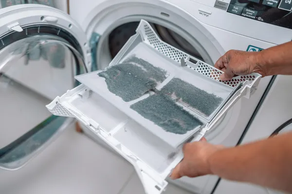 Manos sostienen un filtro lleno de pelusa simbolizando como limpiar filtro de lavadora Samsung para su buen funcionamiento.