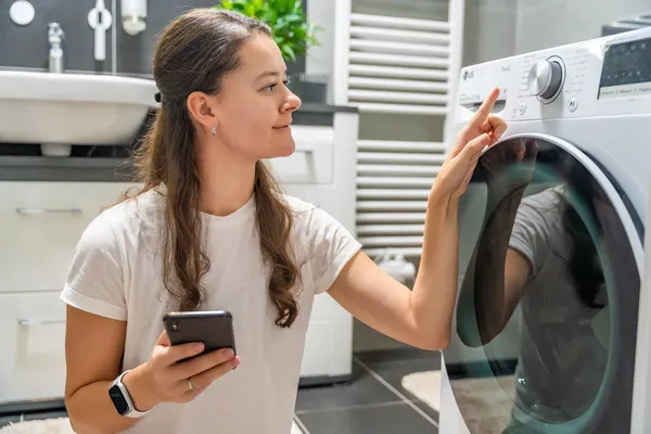 Mujer buscando en su móvil una solución al ver el código de error LE LG en el panel de su lavadora de carga frontal.