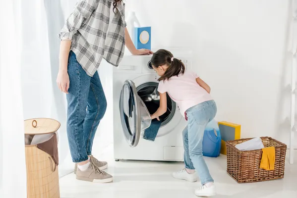 Niña aprende a lavar ropa, un paso clave para evitar sobrecargas y fallas comunes en lavadoras Samsung.
