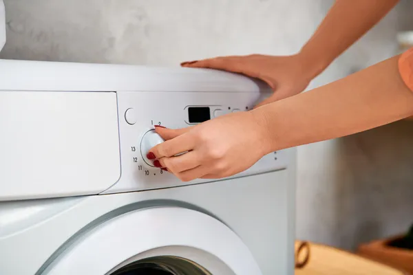 Mujer ajustando el dial de ciclos, un paso esencial al aprender cómo reparar un reloj de lavadora Mabe de tipo análogo.