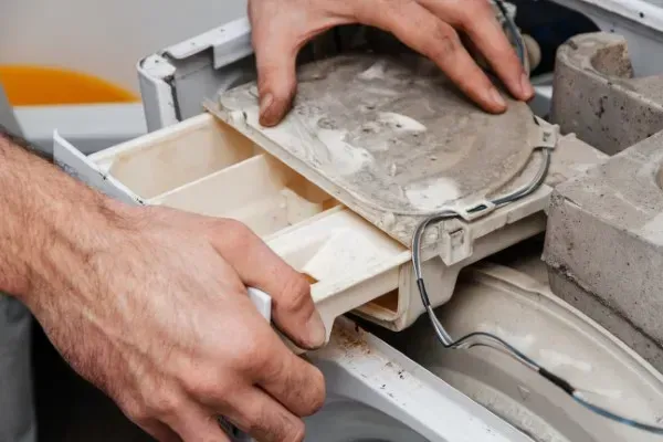 Primer plano de las manos de un técnico retirando el cajón dispensador de detergente realizando reparación de lavadora Whirlpool CDMX