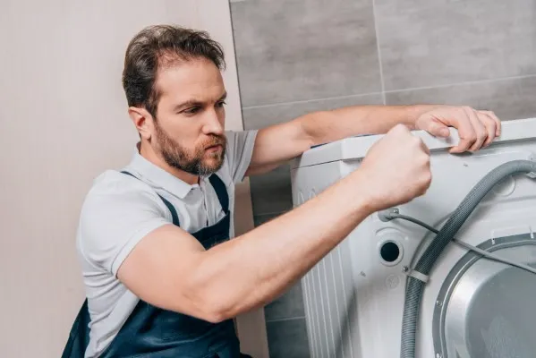 Hombre concentrado inspeccionando las mangueras traseras. Soluciones a como arreglar mi lavadora si no desagua bien.