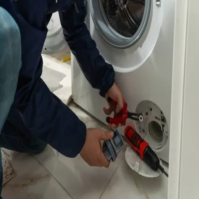 Una persona arrodillada usa pinzas rojas como parte de reparación de lavadora Whirlpool en CDMX.